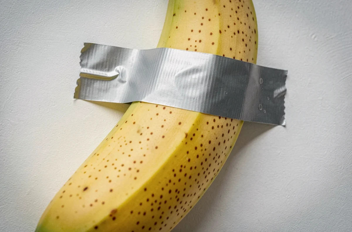 Gros plan sur une banane scotchée au mur avec du ruban adhésif argenté, détail texturé de l'œuvre d'art conceptuel Comedian de Cattelan