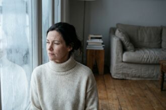 Femme regardant par une fenêtre givrée en hiver, illustrant la perception visuelle par faible luminosité hivernale
