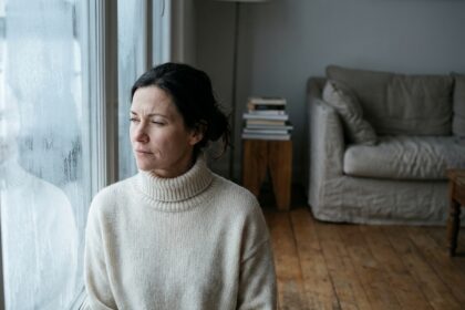 Femme regardant par une fenêtre givrée en hiver, illustrant la perception visuelle par faible luminosité hivernale